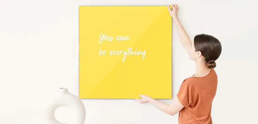 A girl is hanging a yellow glass whiteboard on the white wall.
